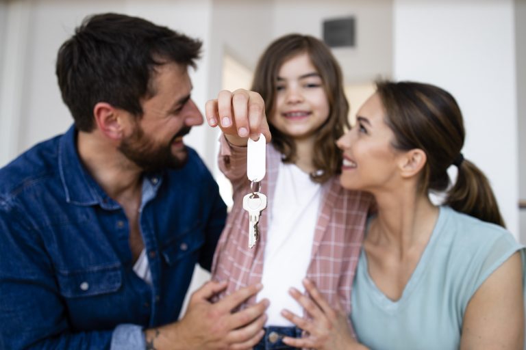 Portrait of smiling caucasian family with daughter holding keys of their new home.